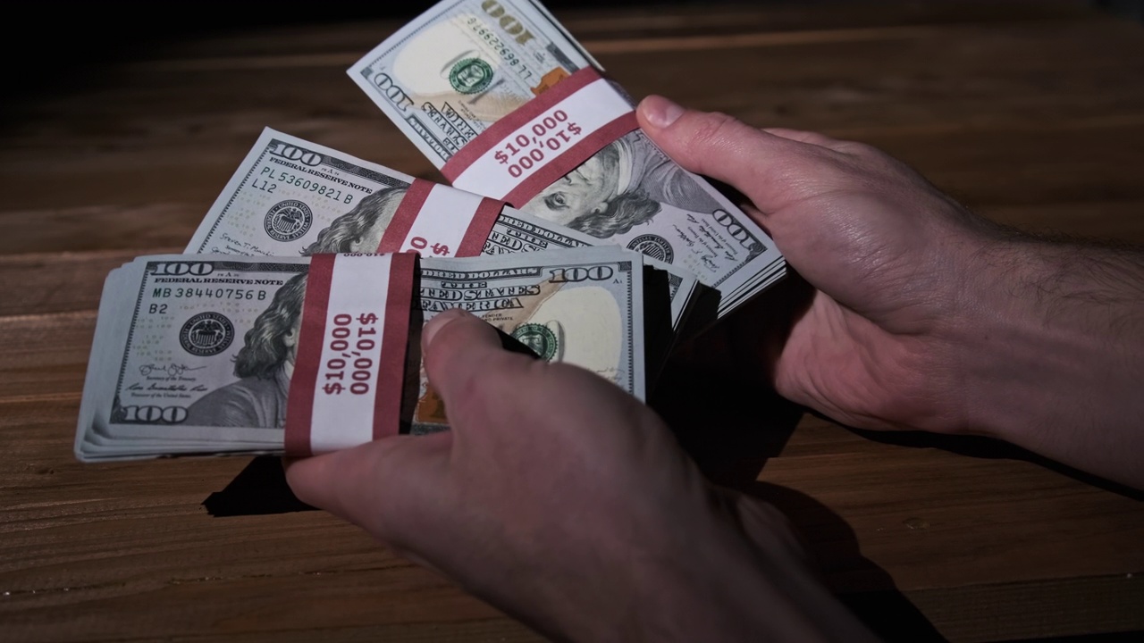 男性的手在木制背景上持有三叠10000美元的钞票视频素材