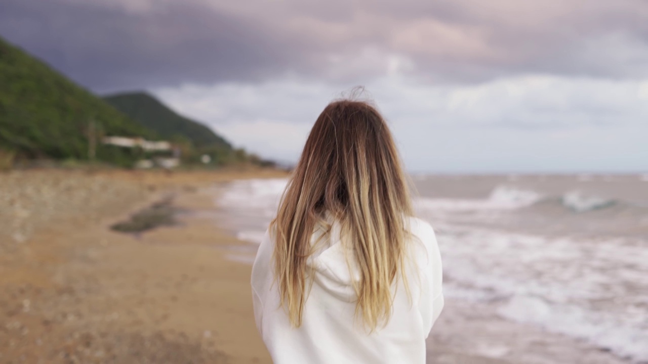 金发女人沿着海岸散步的后视镜肖像，通过电话交谈视频素材