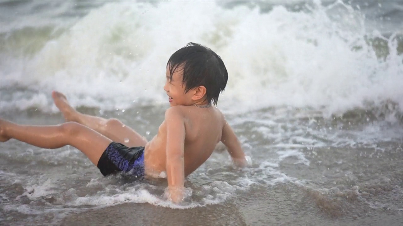 慢镜头拍摄的亚洲男孩在沙滩上享受和玩海和沙子视频素材