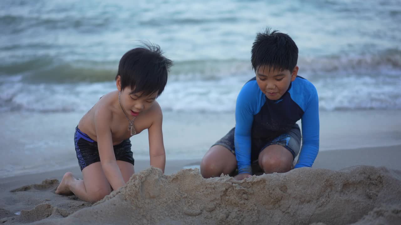 亚洲男孩兄弟在日落时分的海滩上享受和玩海和沙子视频素材