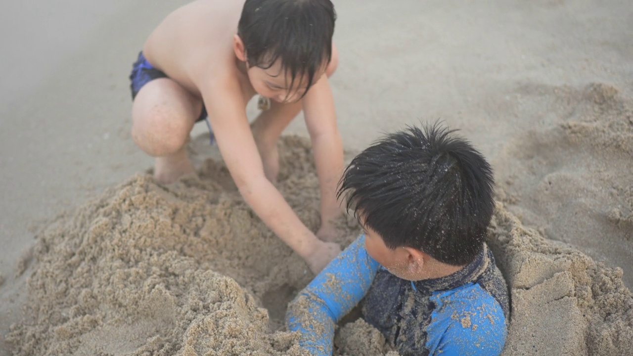 亚洲男孩兄弟在日落时分的海滩上享受和玩海和沙子视频素材