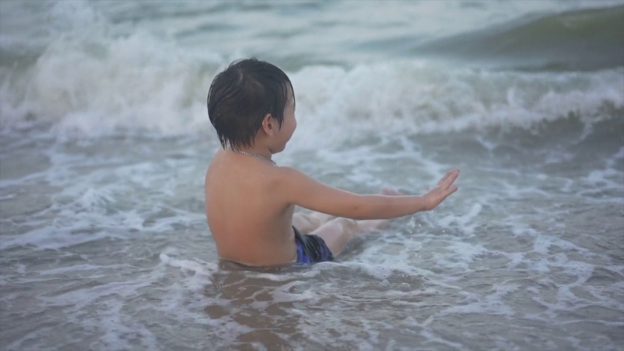 日落时分，亚洲男孩在海滩上享受和玩海和沙子视频素材