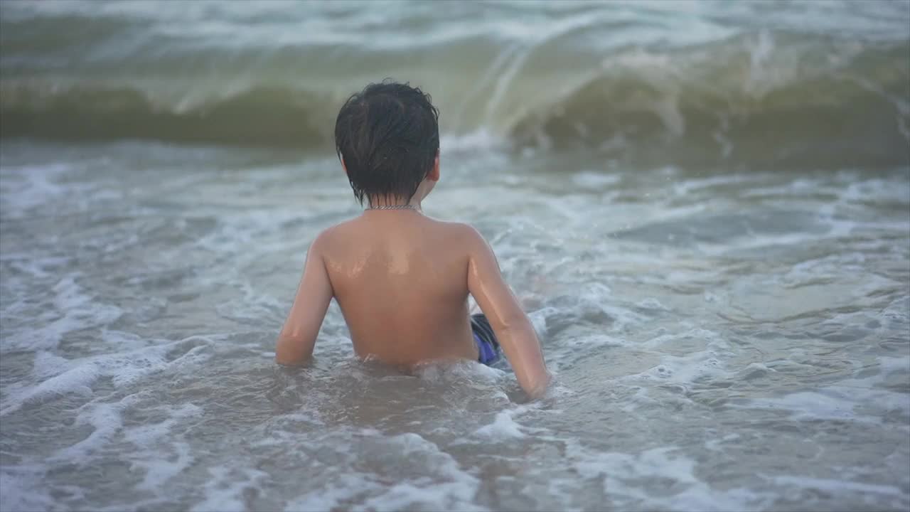 日落时分，亚洲男孩在海滩上享受和玩海和沙子视频素材