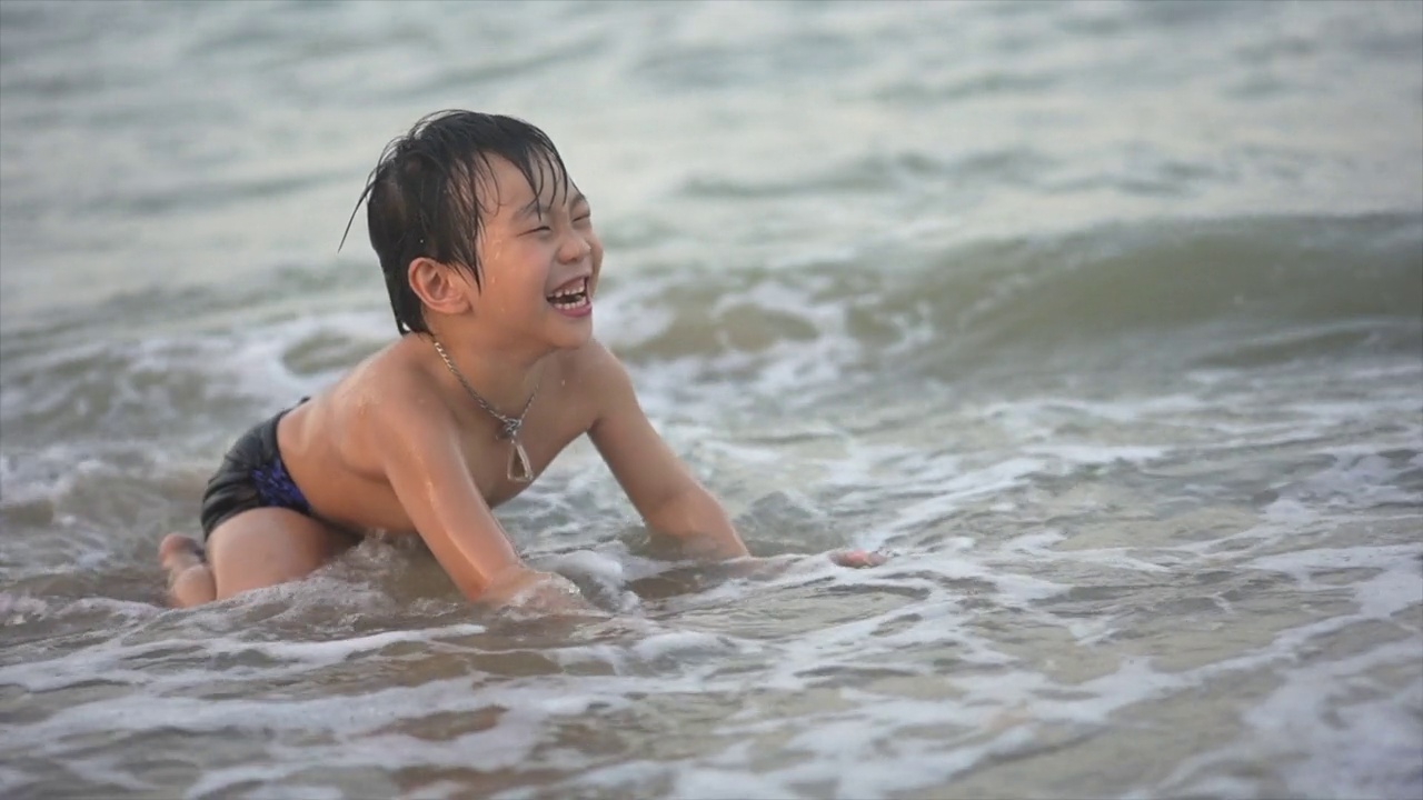 日落时分，亚洲男孩在海滩上享受和玩海和沙子视频素材