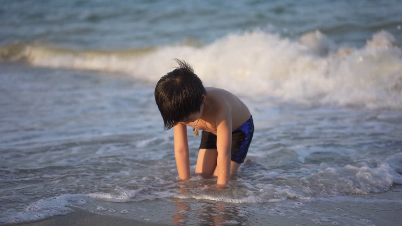 日落时分，亚洲男孩在海滩上享受和玩海和沙子视频素材