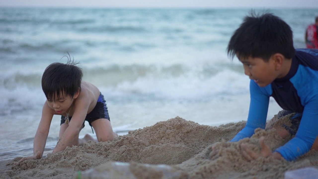 亚洲男孩兄弟在日落时分的海滩上享受和玩海和沙子视频素材