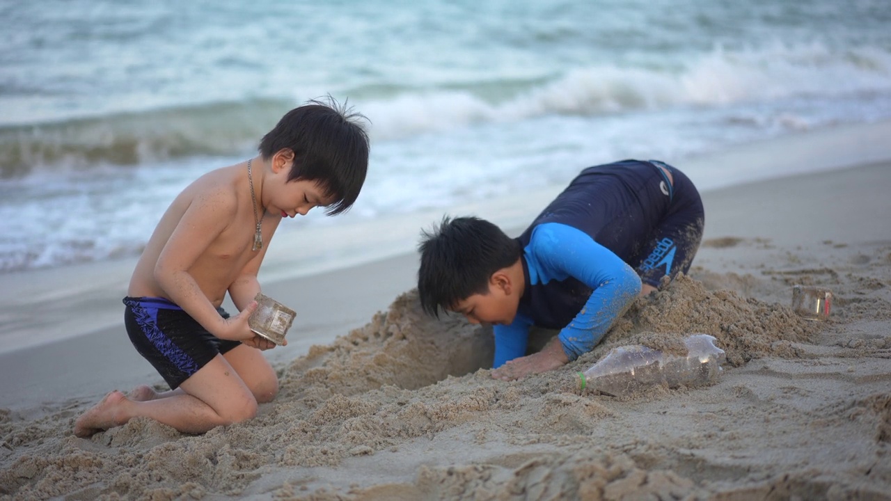 亚洲男孩兄弟在日落时分的海滩上享受和玩海和沙子视频素材