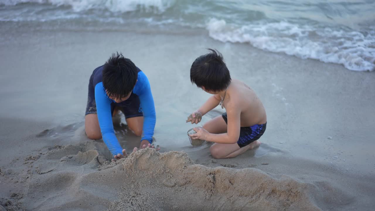 亚洲男孩兄弟在日落时分的海滩上享受和玩海和沙子视频素材