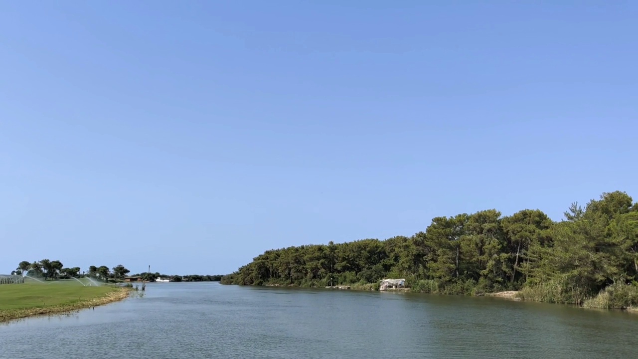 从一艘沿着平静的河流航行的船上拍摄，还有岸边的树木和高尔夫球场视频素材