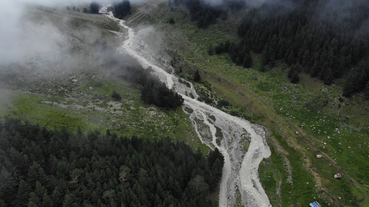 空中俯瞰被绿色的高山森林包围的河流在一个多云的日子与雾和低云。神秘谷4k的低空飞行概述视频下载