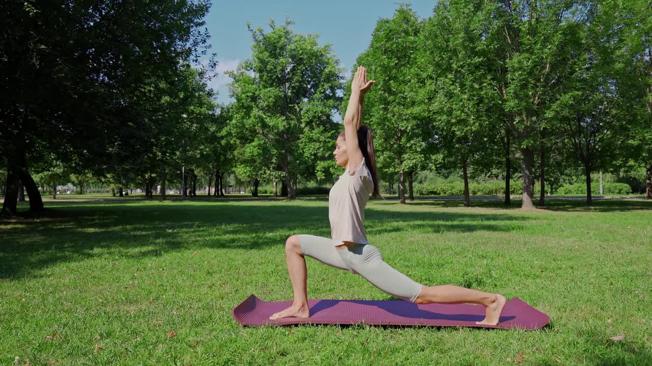 一个年轻的女人站在瑜伽垫上。在一个阳光明媚的日子里，在公园的绿色草地上练习瑜伽。瑜伽,练习冥想。瑜伽课程的性质。拉伸、普拉提视频素材