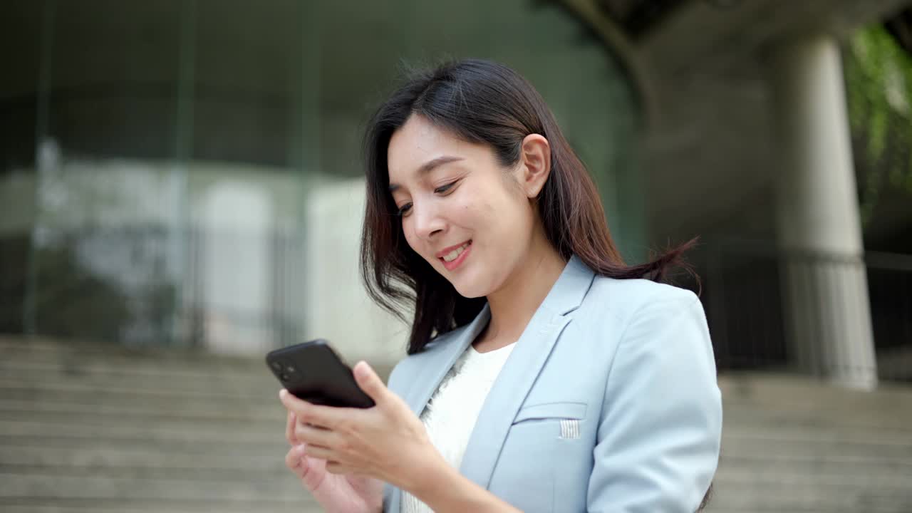 聪明的女性使用手机进行商务交流。漂亮的女商人用手机在市中心的建筑物里玩社交媒体。智能手机的概念。视频素材