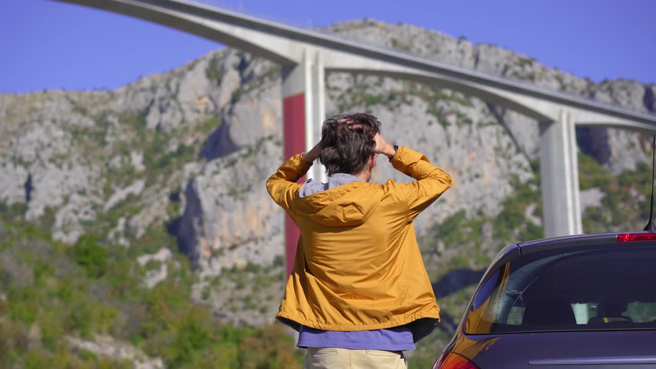 在黑山，一名男子站在他的车旁看着莫拉西卡桥。他对这座桥的造价和黑山欠中国的钱感到震惊视频素材