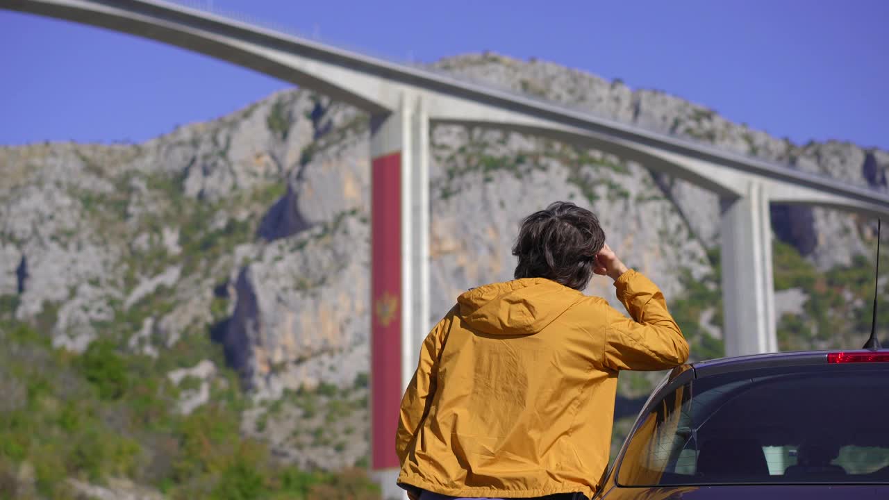 在黑山，一名男子站在他的车旁看着莫拉西卡桥。他正在作一次穿越黑山的汽车旅行视频素材