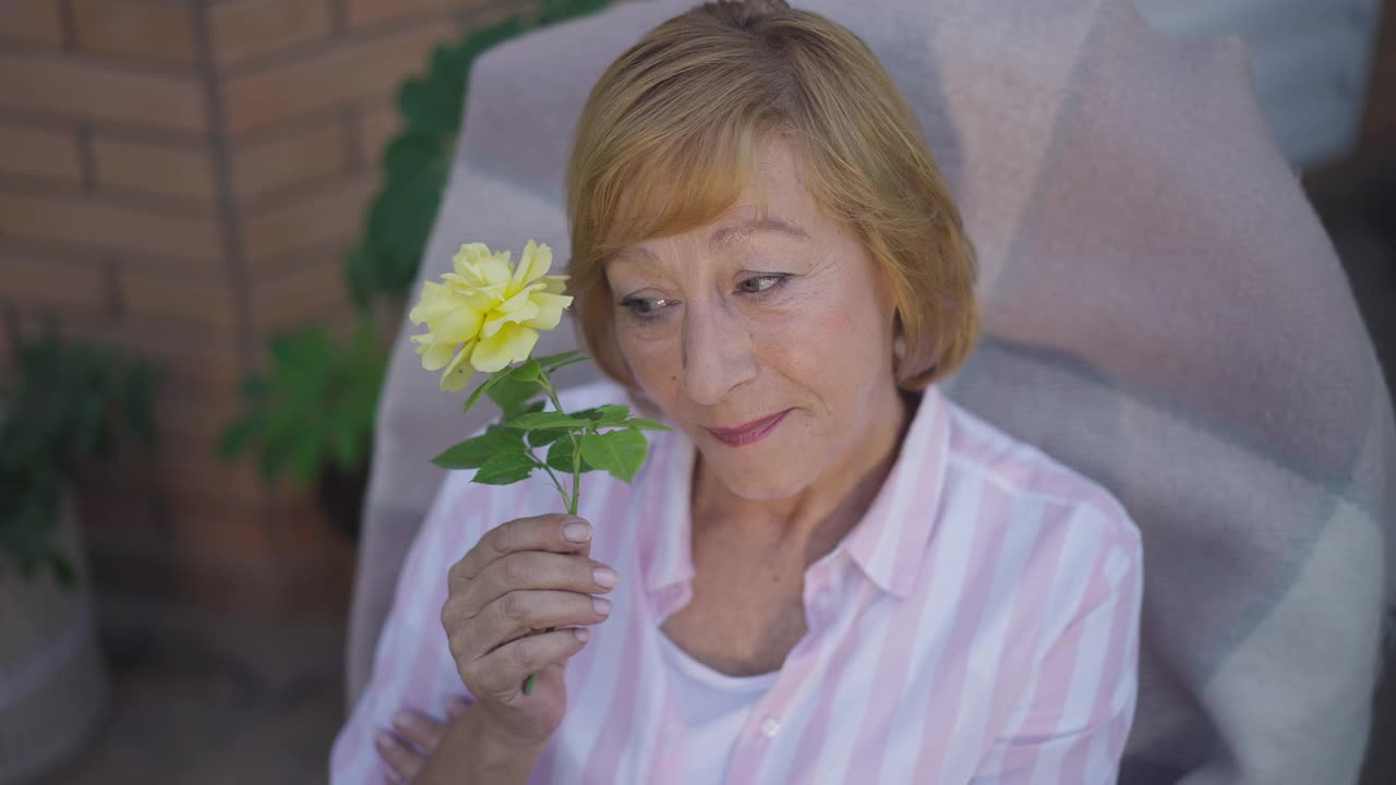 微笑的快乐的女人坐在黄色的玫瑰看着相机的肖像。放松的白人女性退休与花在户外的慢动作摆姿势。生活方式和幸福理念。视频素材