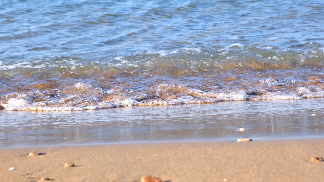 夏日阳光明媚的一天，沙滩上蔚蓝的大海的轻柔波浪视频素材