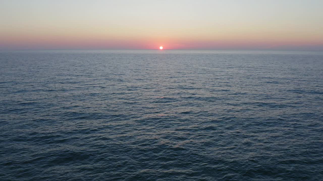 夕阳西下，天空泛着橘黄色，海浪平静的海面上的空中飞行。视频素材