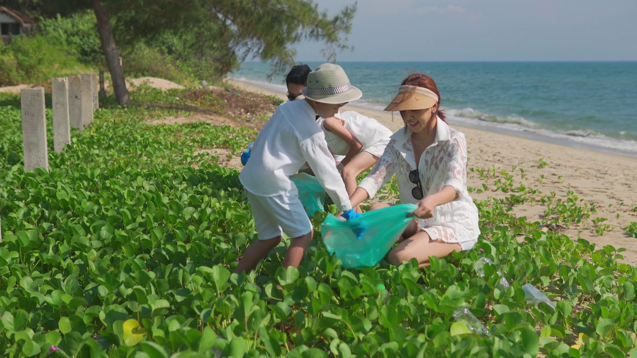 幸福的亚洲家庭带着垃圾袋一起在沙滩上清洁区域。视频素材