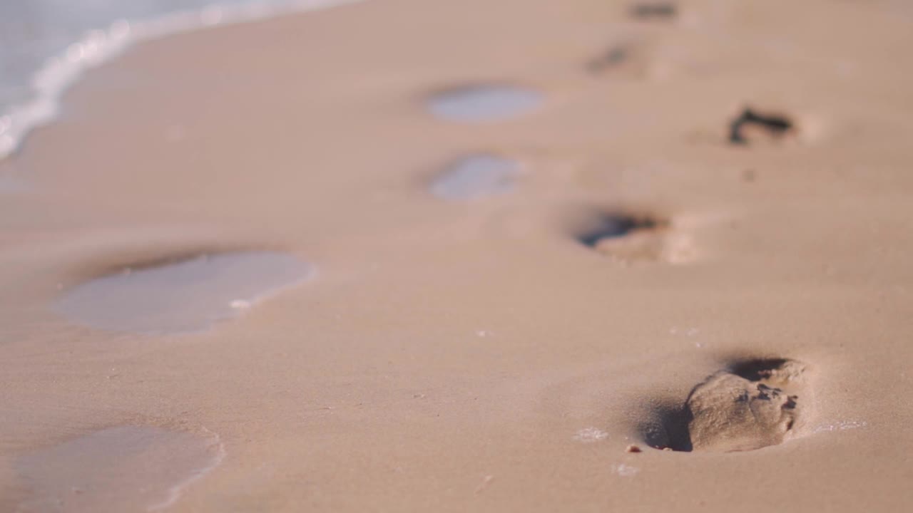 沙滩上的脚步被海浪冲走的特写，沙滩背景。假日概念，暑假在海滩度假的背景。视频素材