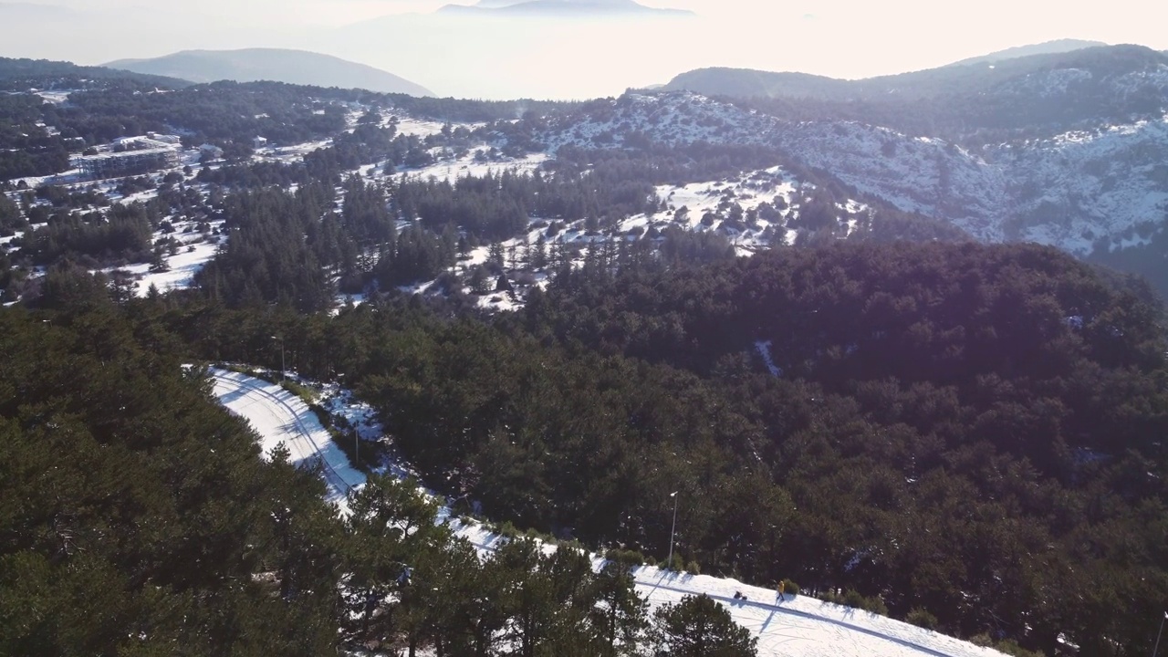 飞过白雪覆盖的道路和松树，还有山丘和云彩。视频素材