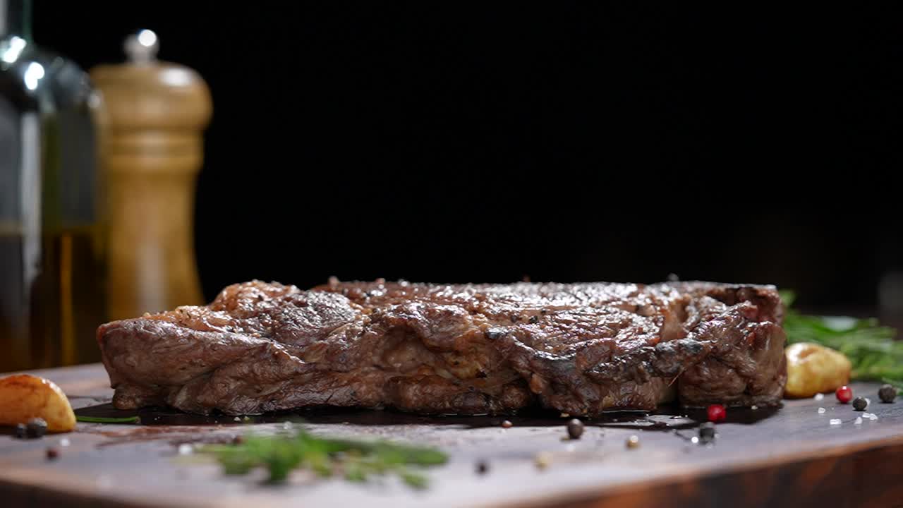 煮熟多汁的牛排，肉，牛肉和调味料掉在木砧板上。慢动作视频素材