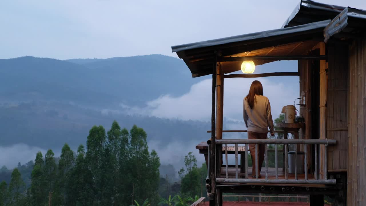 一个女人在木制房子的阳台上喝饮料，在雾天可以看到美丽的山景视频素材