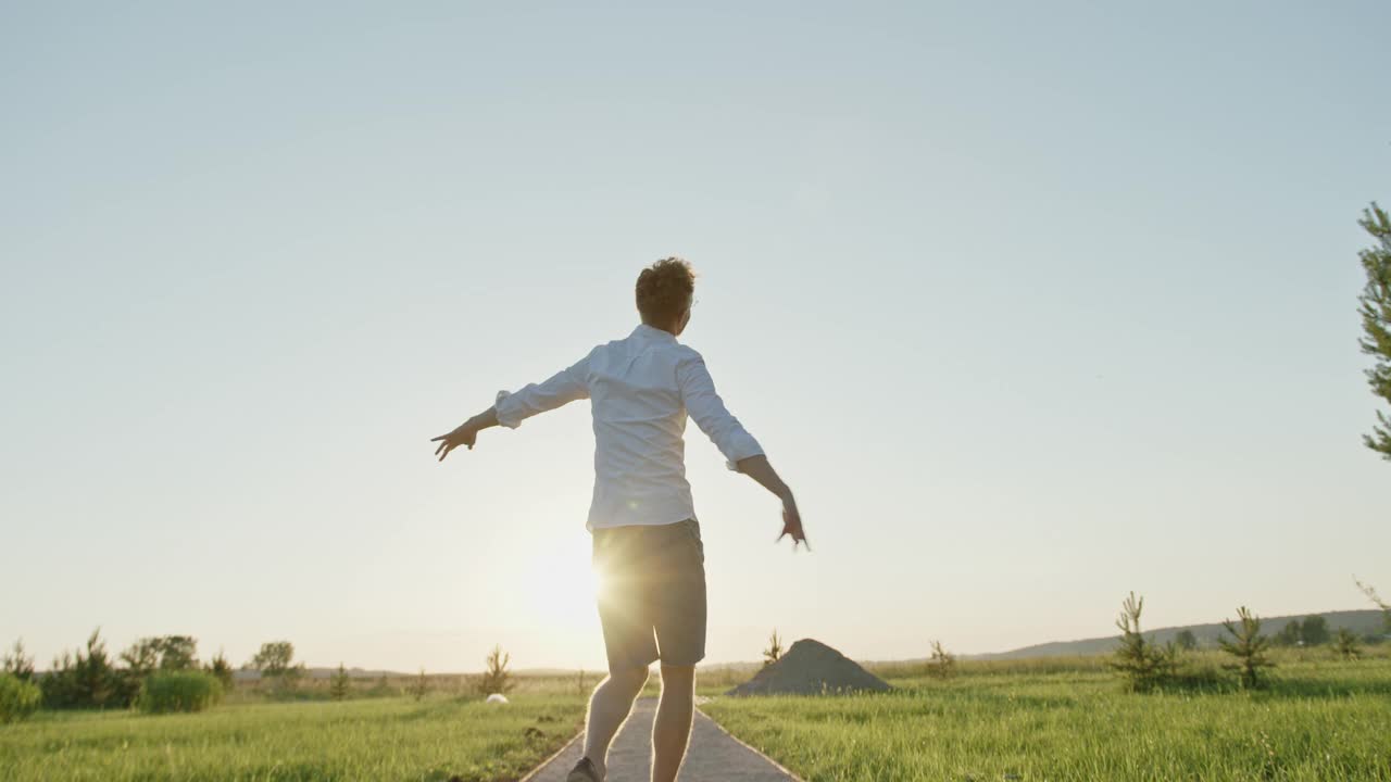 跟踪拍摄的快乐的年轻男性走在小路上，在日落的天空下打着手势视频下载