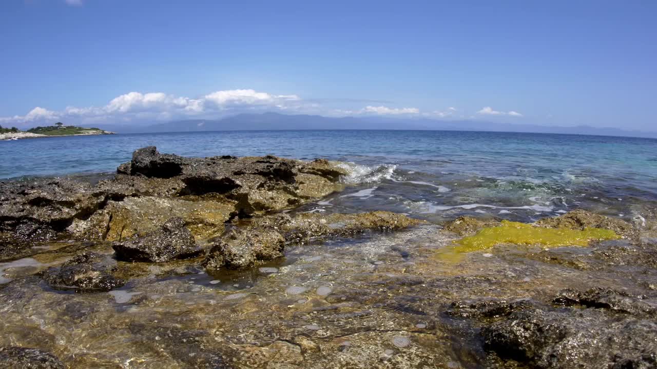 海浪冲击着岩石海岸，远处你可以看到覆盖着大片森林的山脉视频素材