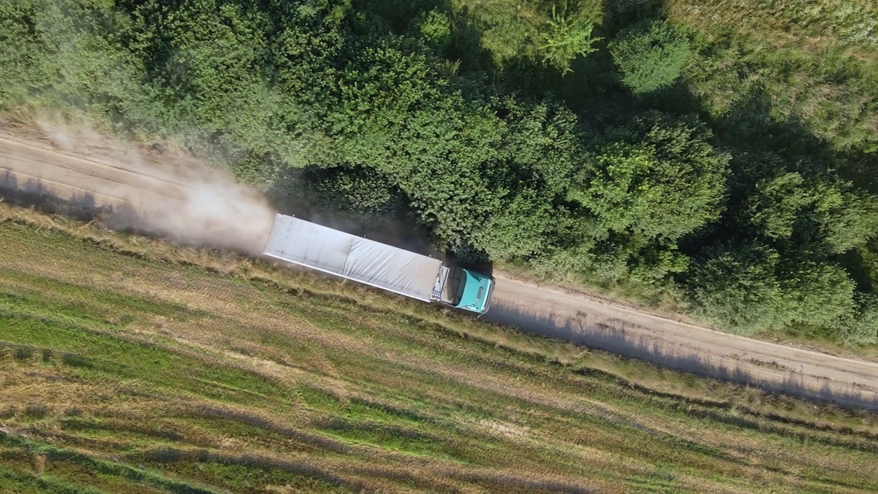 从空中俯瞰，卡车在农田麦田之间的土路上行驶，扬起了大量的尘土。在收获季节用联合收割机收获后的谷物运输视频素材