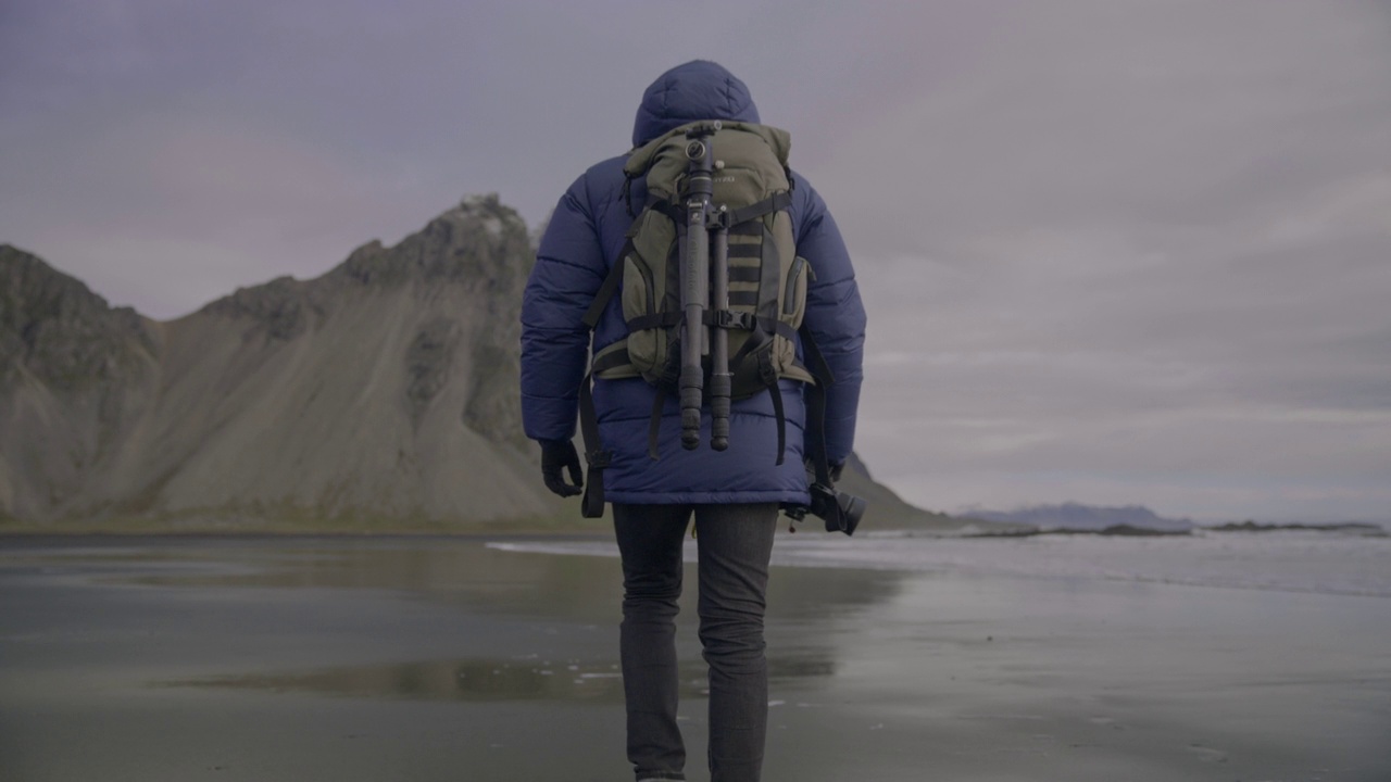 带着相机的徒步旅行者走过潮湿的海滩，走向维斯特拉霍恩山视频素材