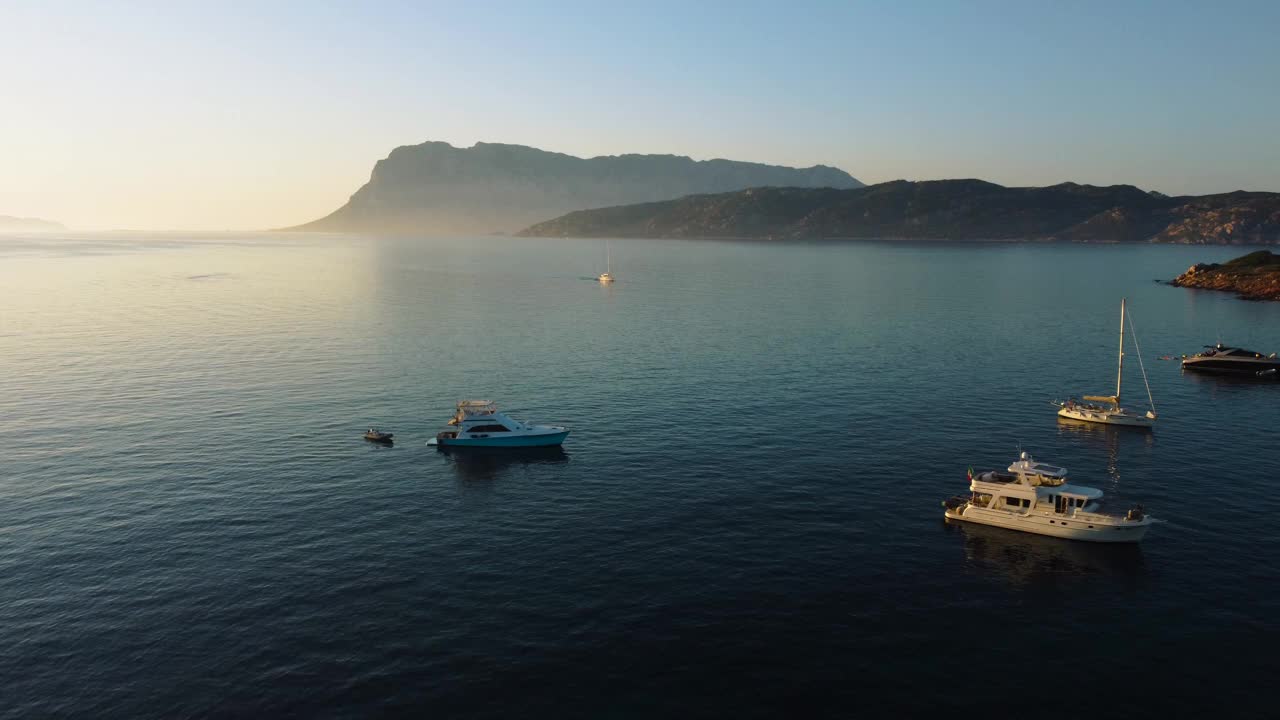 风景如画的撒丁岛，清澈的蓝色绿松石和平静的海水在意大利的天然沙滩海岸海湾与太阳和帆船。空中无人机在度假岛屿上的旅游度假目的地进行空中飞行。视频素材