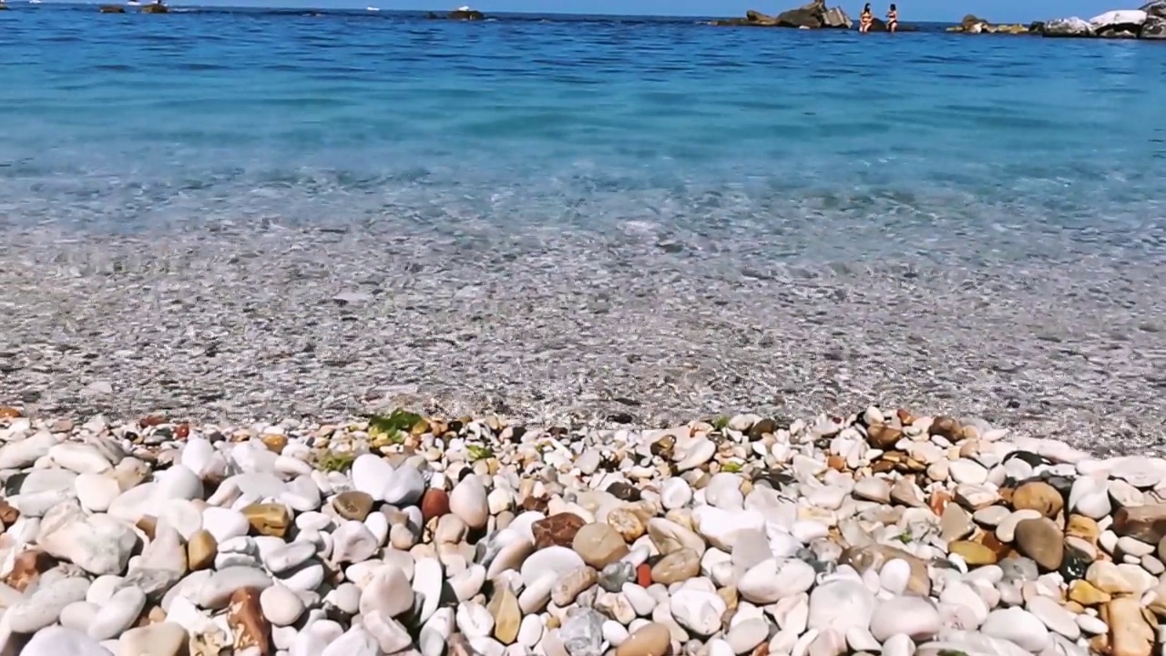 沙滩上有彩色的鹅卵石，阳光明媚的日子里有海浪视频素材