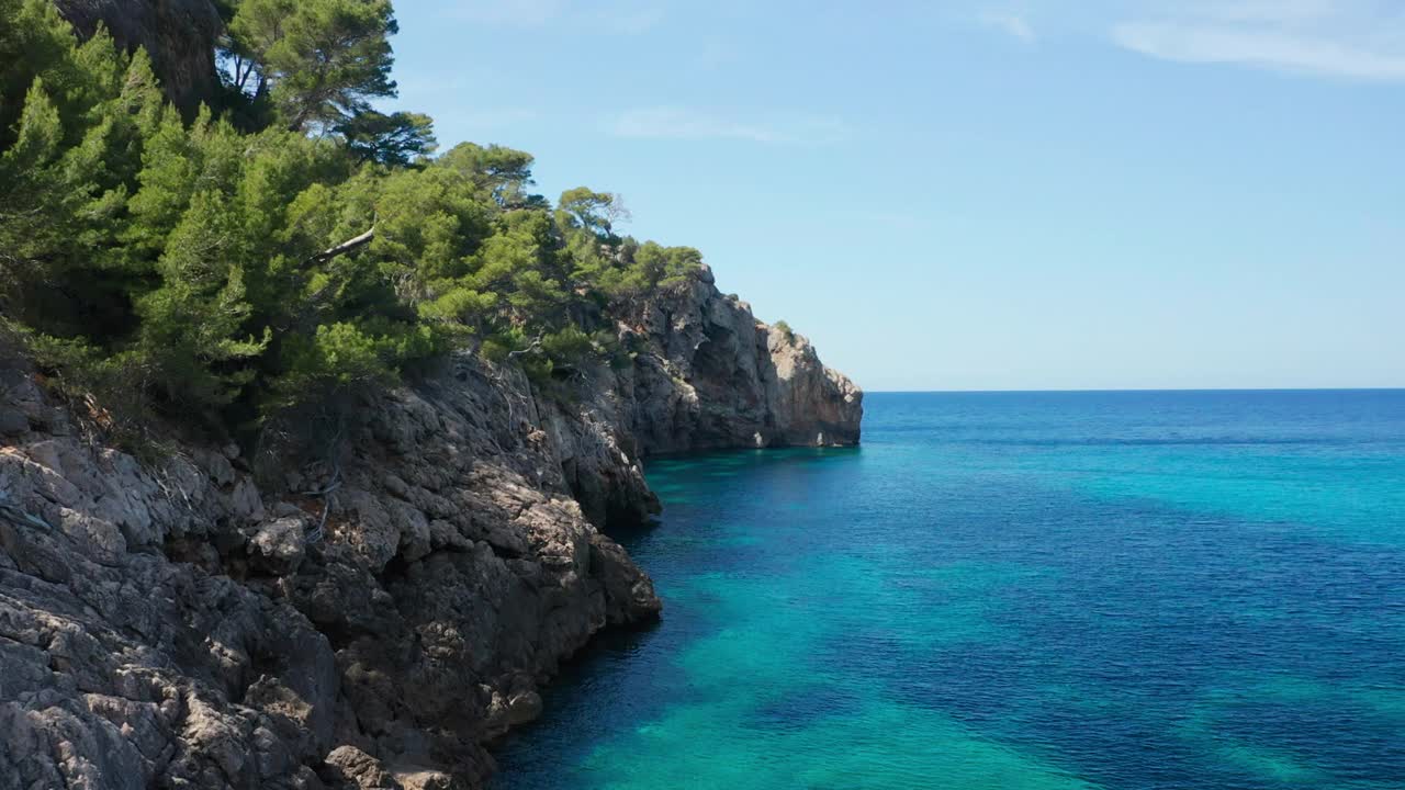 无人机在岩石海岸线和树木，蓝色，宁静的大海上飞行视频素材