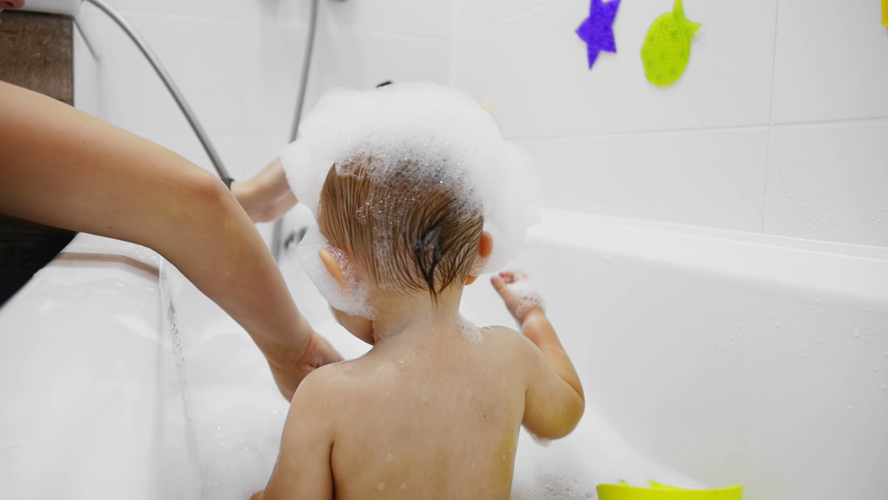 一个胖乎乎的孩子头上沾着泡沫，在白色的浴缸里洗澡视频下载