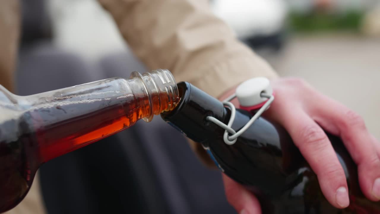一个男人的手从一个瓶子往另一个瓶子里倒啤酒的特写镜头。视频下载
