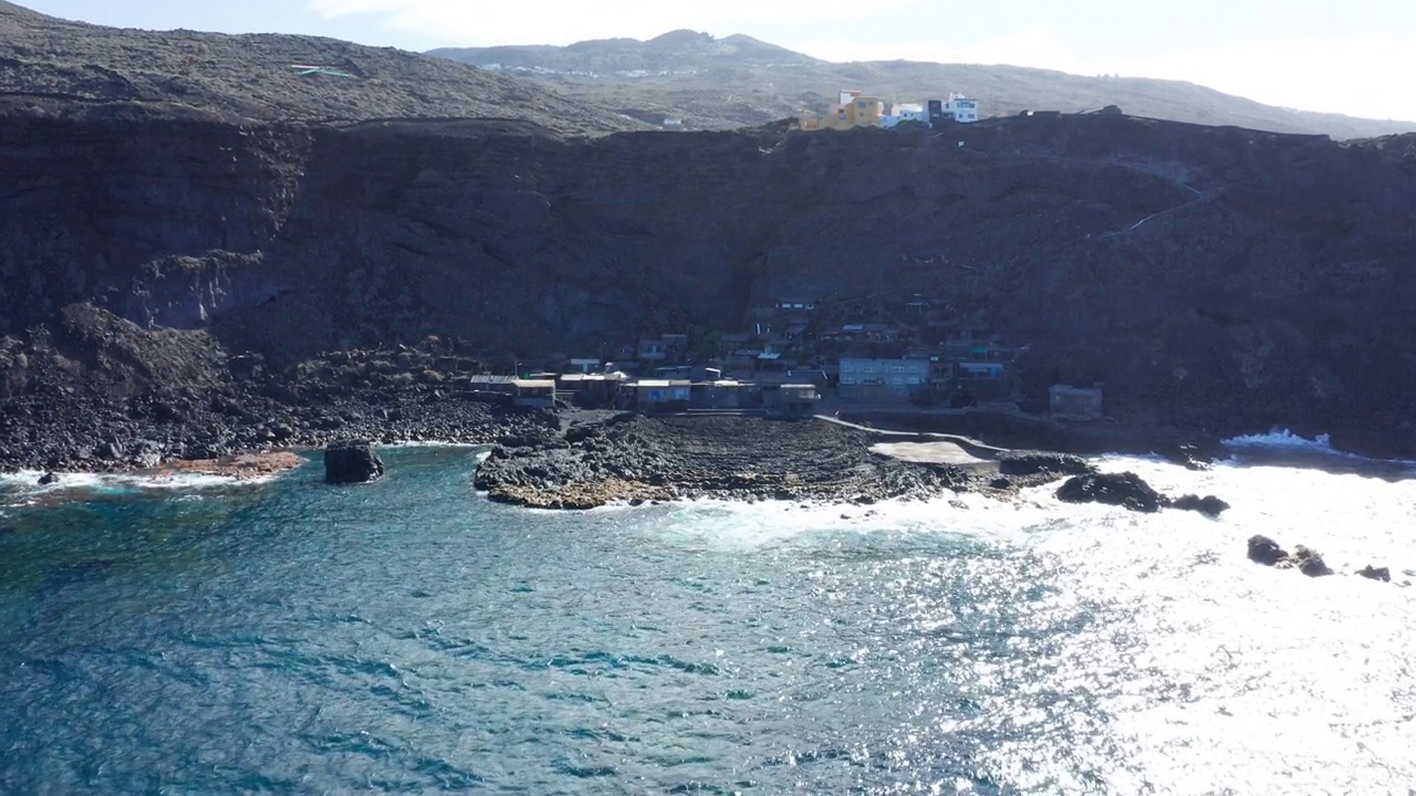 空中摄影车越过海洋，朝着阳光下的岩石湾的小村庄视频素材