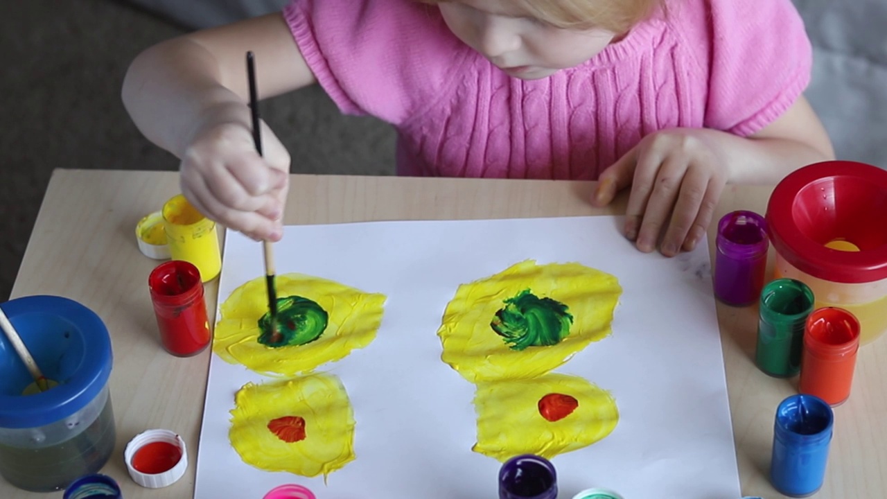 小孩子坐在家里的桌子上，用彩色颜料画画视频素材