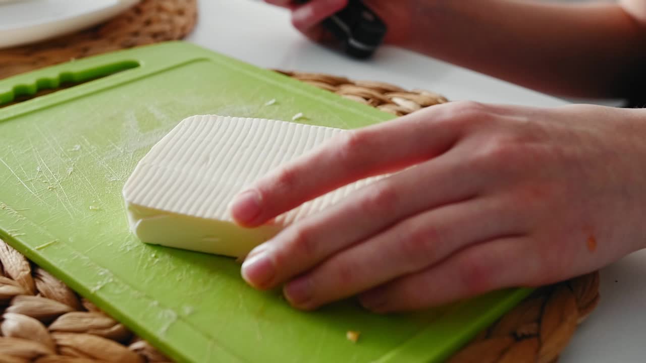 孩子的手在绿色塑料切菜板上切起司视频下载