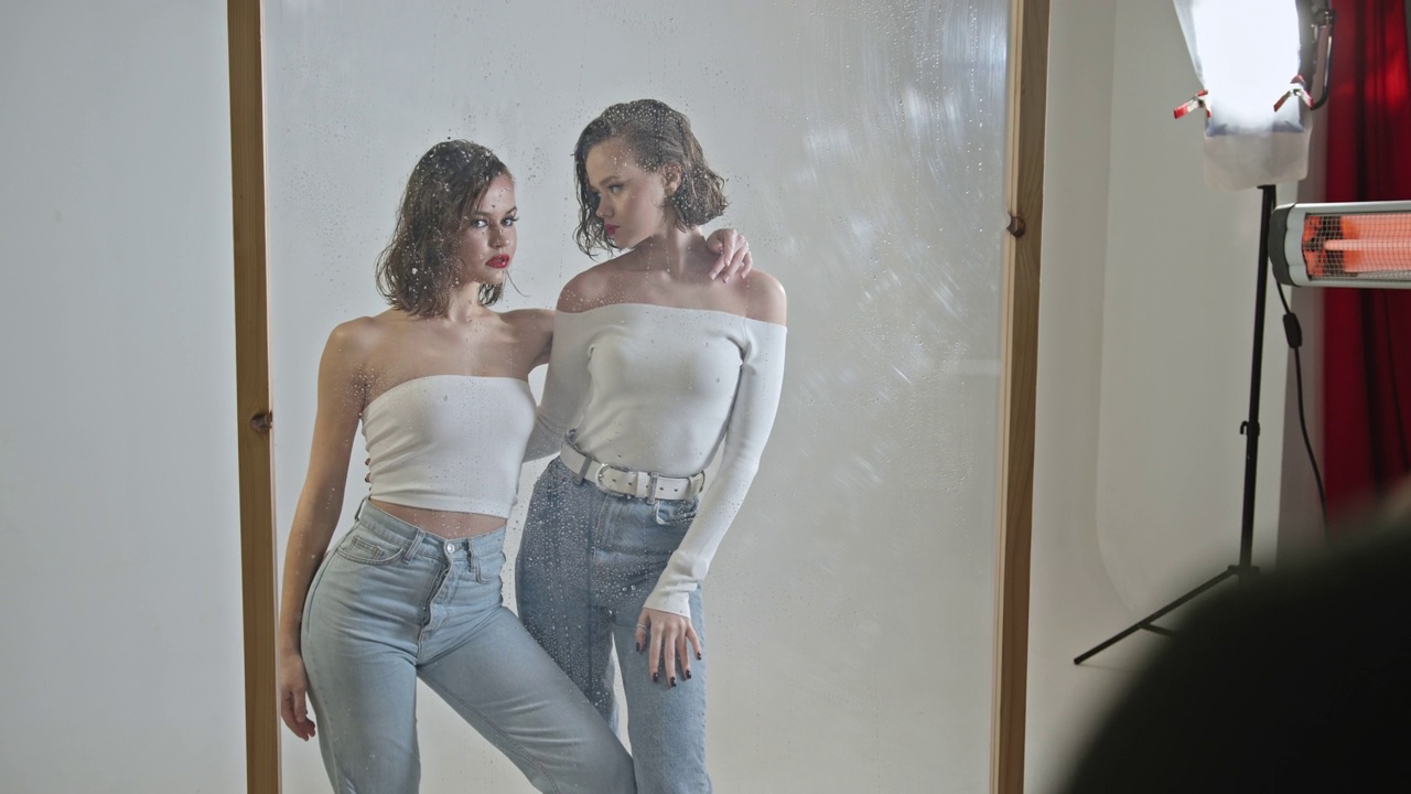两名女孩模特一起摆造型，化妆后的时尚发型，站在玻璃创意摄影师拍摄的摄影工作室后台视频下载