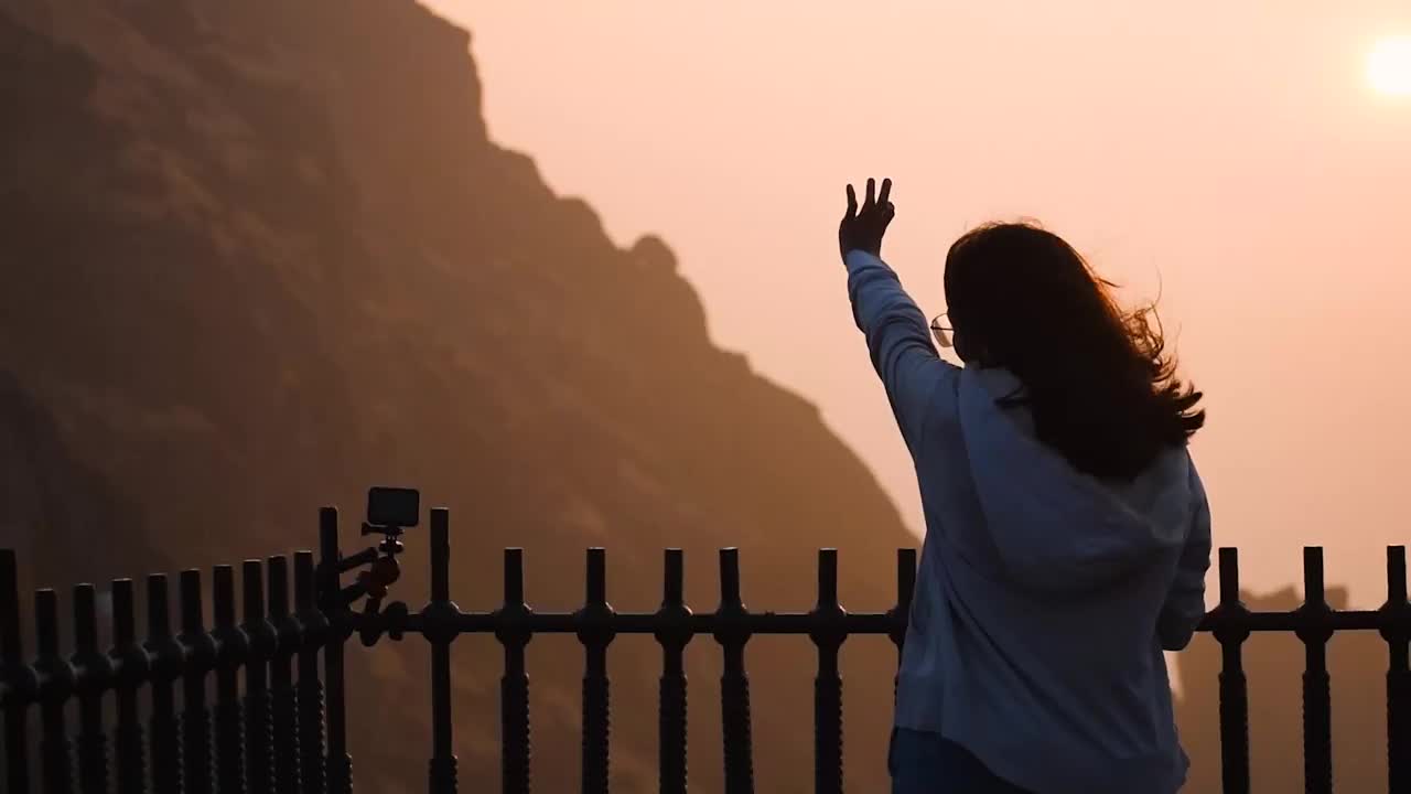 日出时，印度年轻女子在Girnar山上举起手的剪影。女子成功登山，欣赏风景。旅行和冒险的概念视频素材