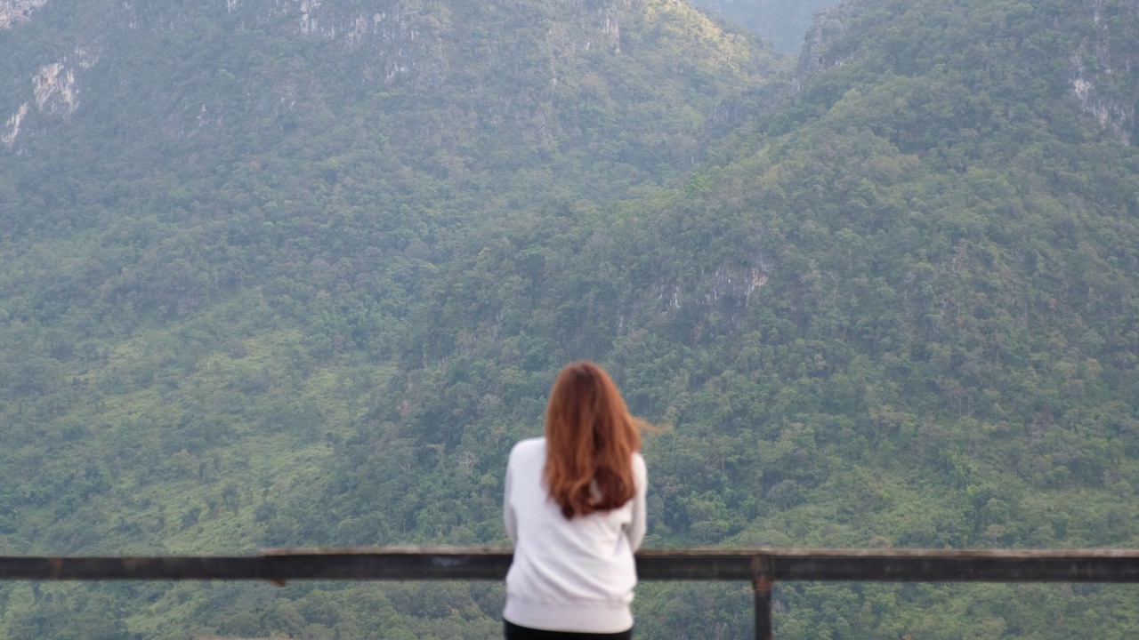 模糊的后视图，一个女性旅行者坐在木制阳台上，看着美丽的山景视频素材