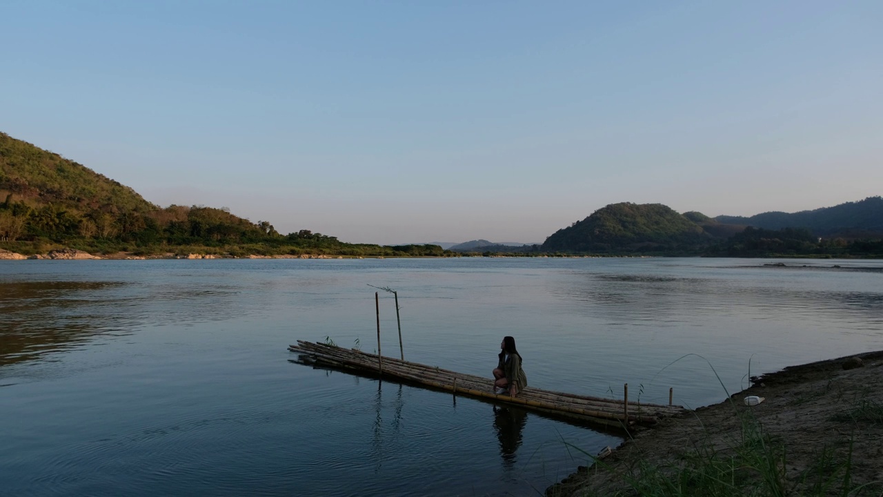 一名年轻的亚洲妇女在湄公河的竹墩上散步、坐着、戏水视频素材