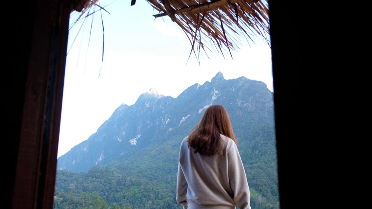 一个女游客走在木房子外面，看着美丽的山景的后视图视频素材