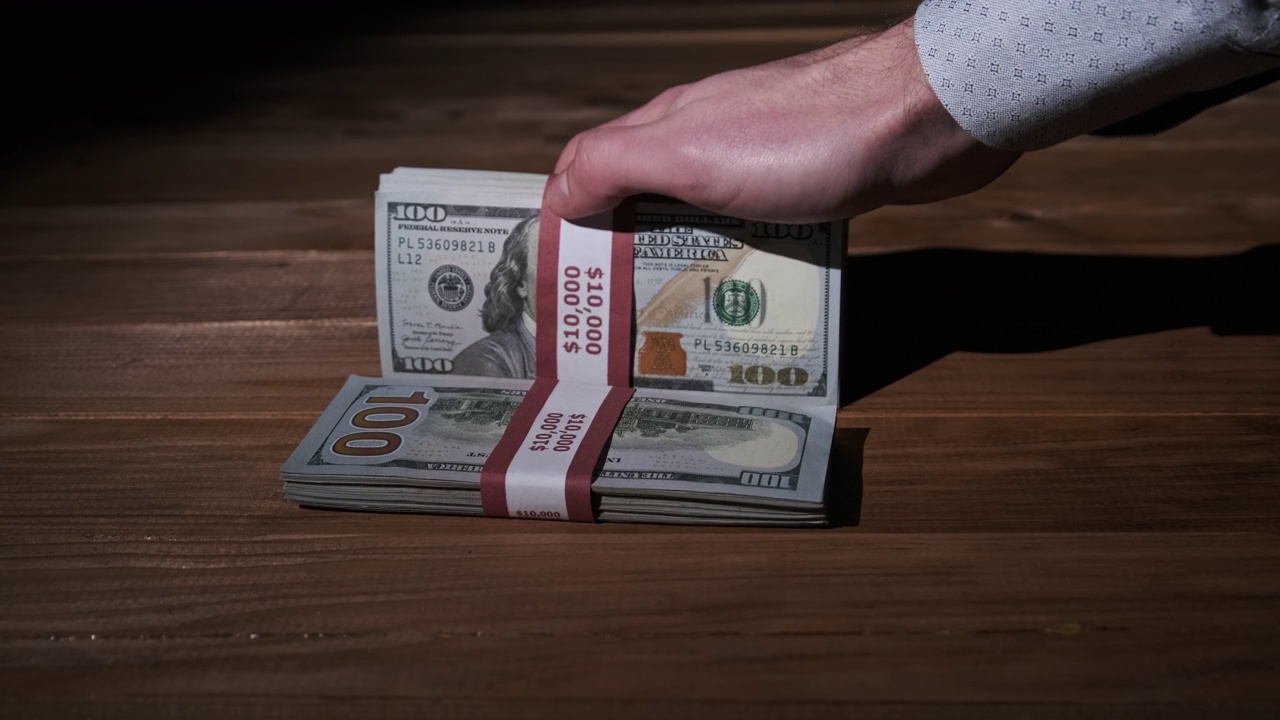 男性的手在木制背景上持有三叠10000美元的钞票视频素材