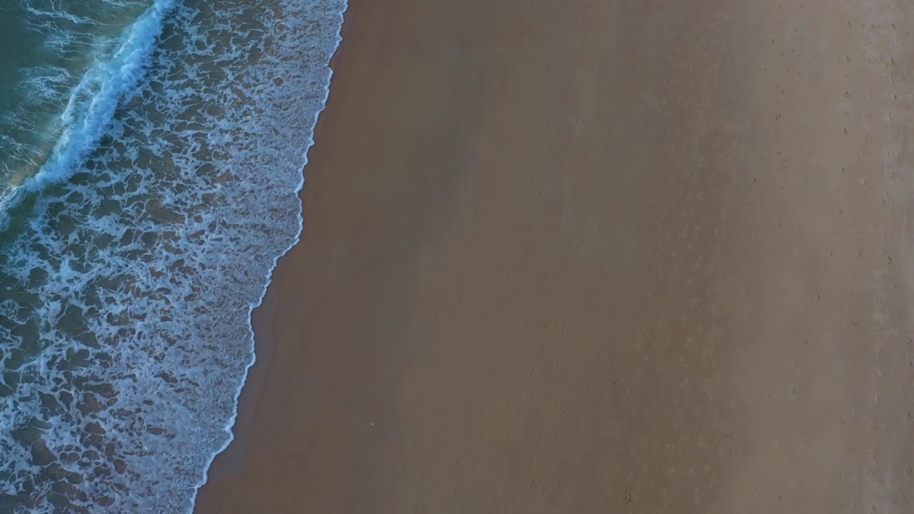 空中俯瞰绿色的海浪拍打在沙滩上。视频素材