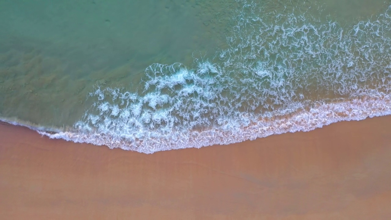 空中俯瞰绿色的海浪拍打在沙滩上。视频素材