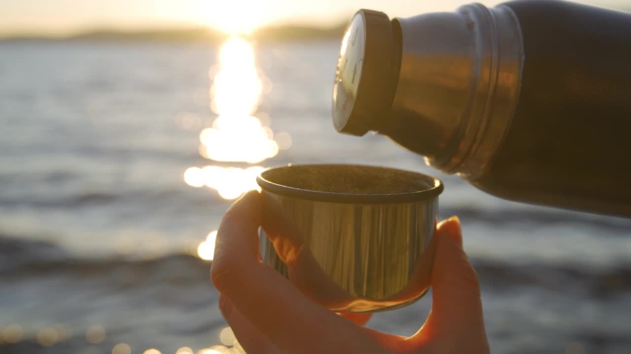 近距离拍摄从暖水瓶中倒茶的营地附近的河流湖。秋天在大自然中旅行视频下载