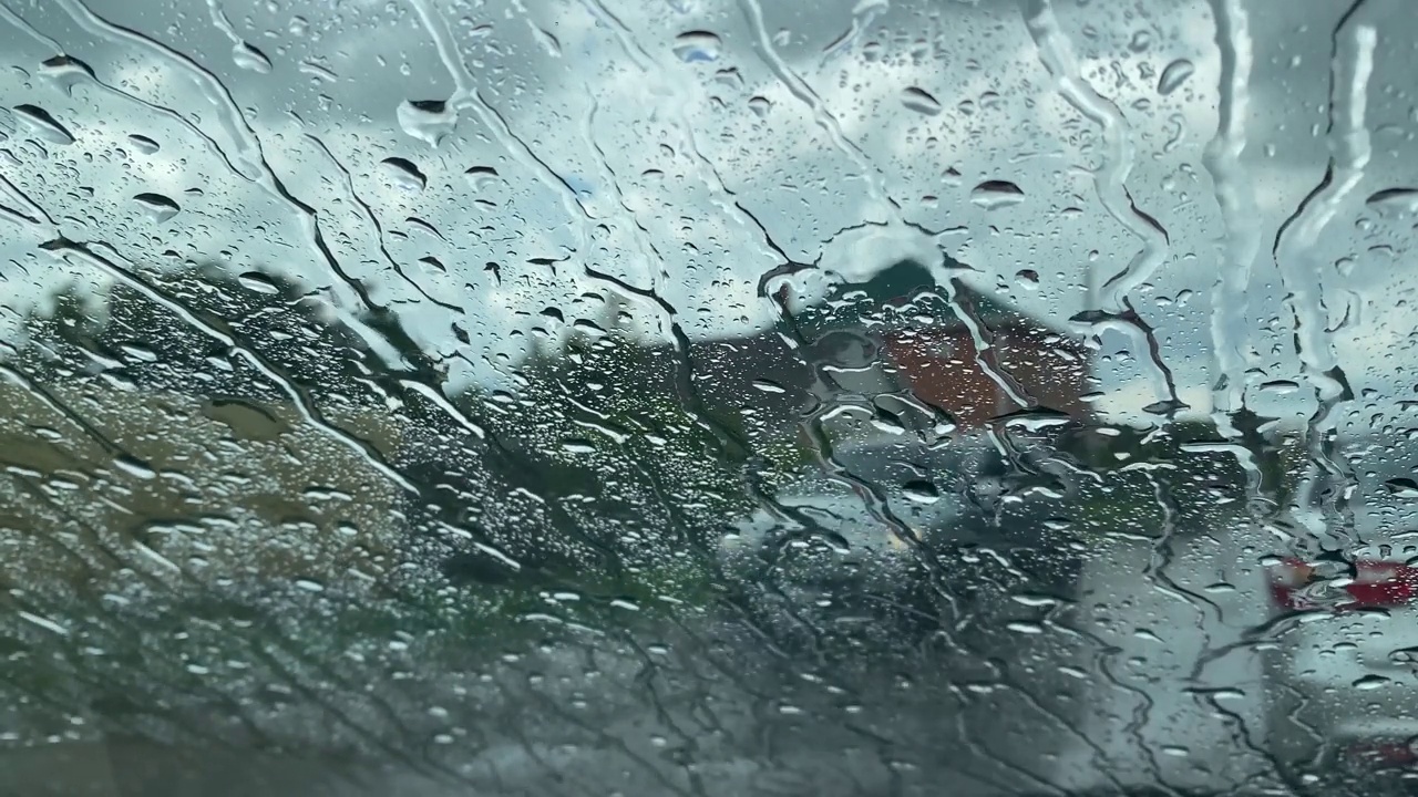 车窗上的雨滴。倾盆大雨。城市和道路穿过一扇潮湿的窗户。多云的一天。视频素材