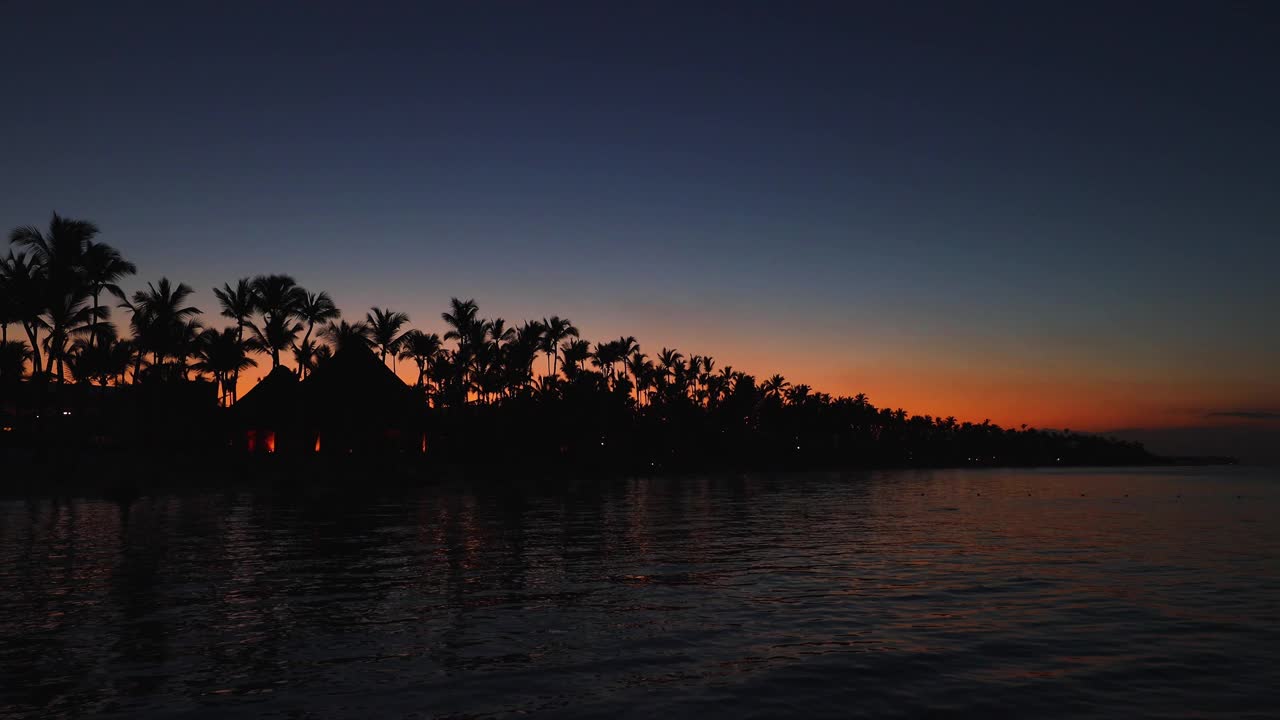 日落时的热带岛屿，棕榈树和海滩平房。浪漫的夜晚，海水上闪烁的灯光。视频素材