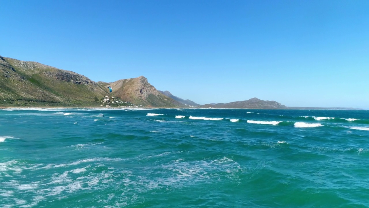 广阔的空中拍摄的孤独的风筝冲浪海浪与山区的背景视频素材